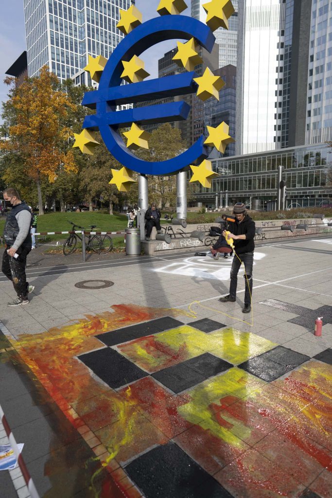 Vor dem Eurozeichen am Willy-Brandt-Platz in Frankfurt malt ein Aktivist am Straßenbild, das Teil des Protests für Klimagerechtigkeit am Weltspartag ist.